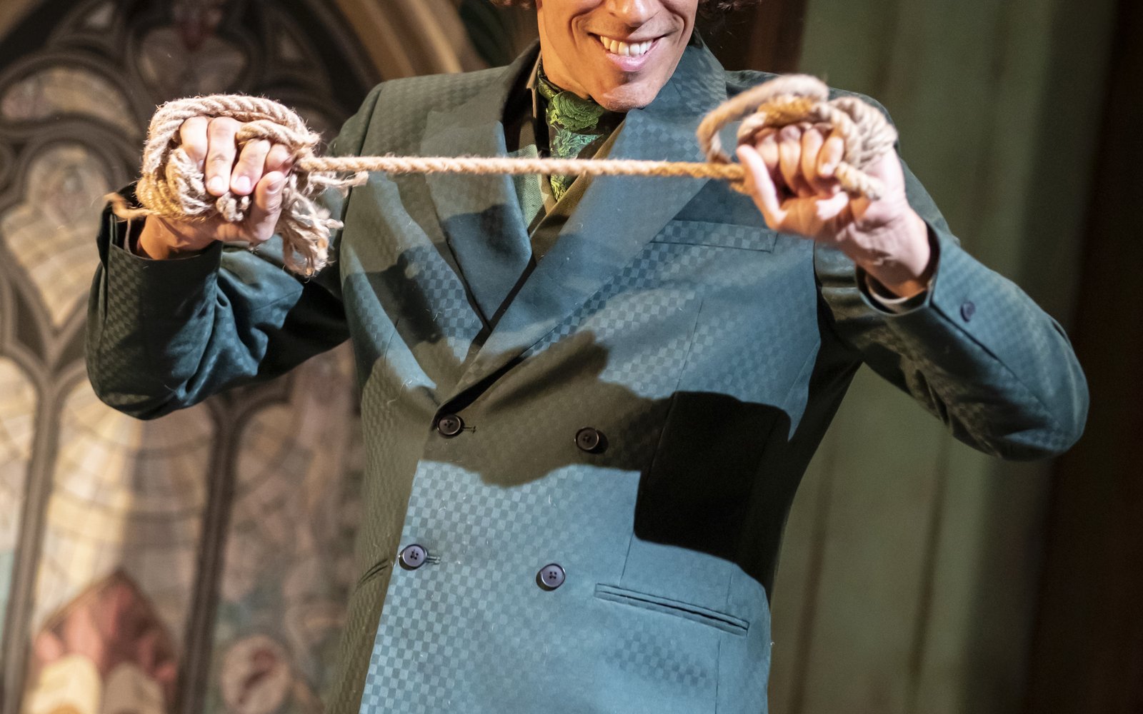 A man in a green suit holds a length of rope between his hands, with each end of the rope wrapped around each hand.