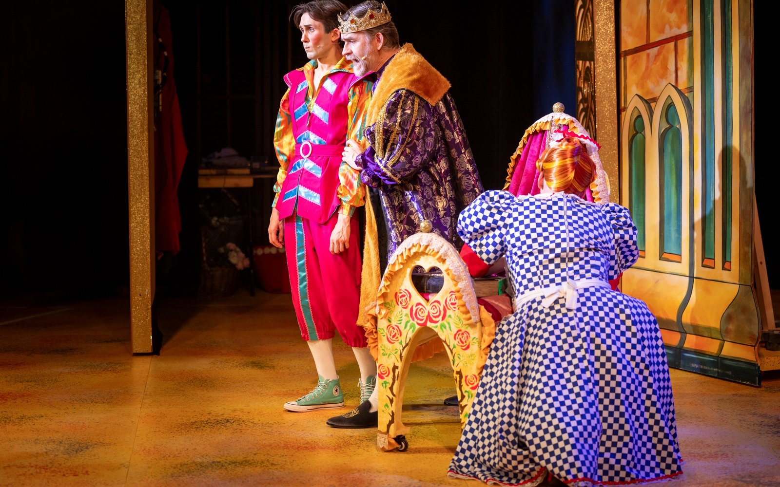 Nanny Nutkins faces away from the camera, kneeling down by a crib. On the other side of the crib stands Happy Harry, looking morose, and King Truman, who is speaking to him.