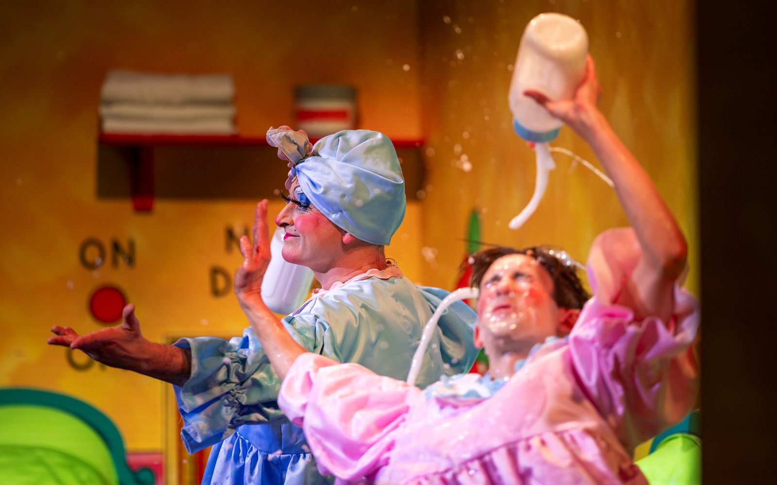 Happy Harry, wearing a pink dress, is mid-fall, with a bottle of milk emptying over his face. In the background, Nanny Nutkins smiles out at the audience with her arms outstretched.