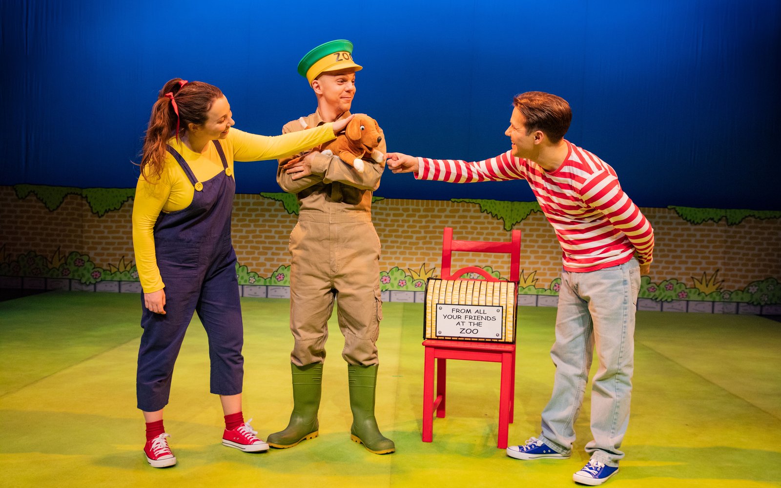 A boy and a girl stand with a zoo keeper, the zoo keeper is holding a small dog in his arms