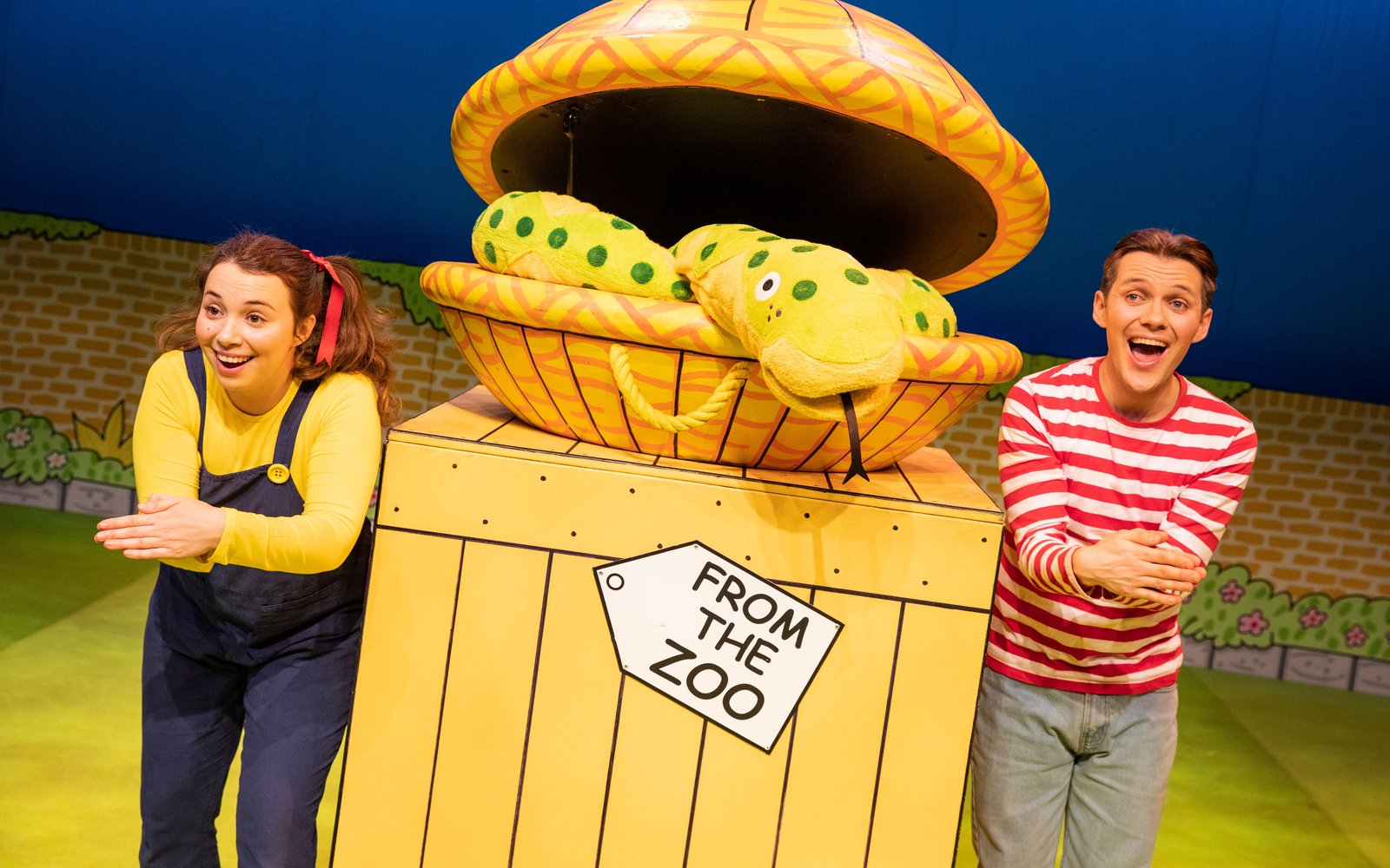 A boy and a girl stand either side of a snake on top of a yellow box