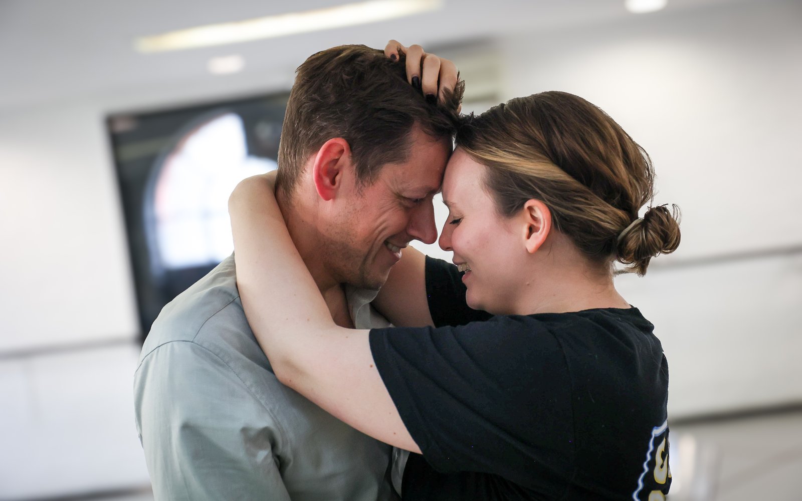 The actors of Sky and Sarah stand with their foreheads touching, smiling at each other.