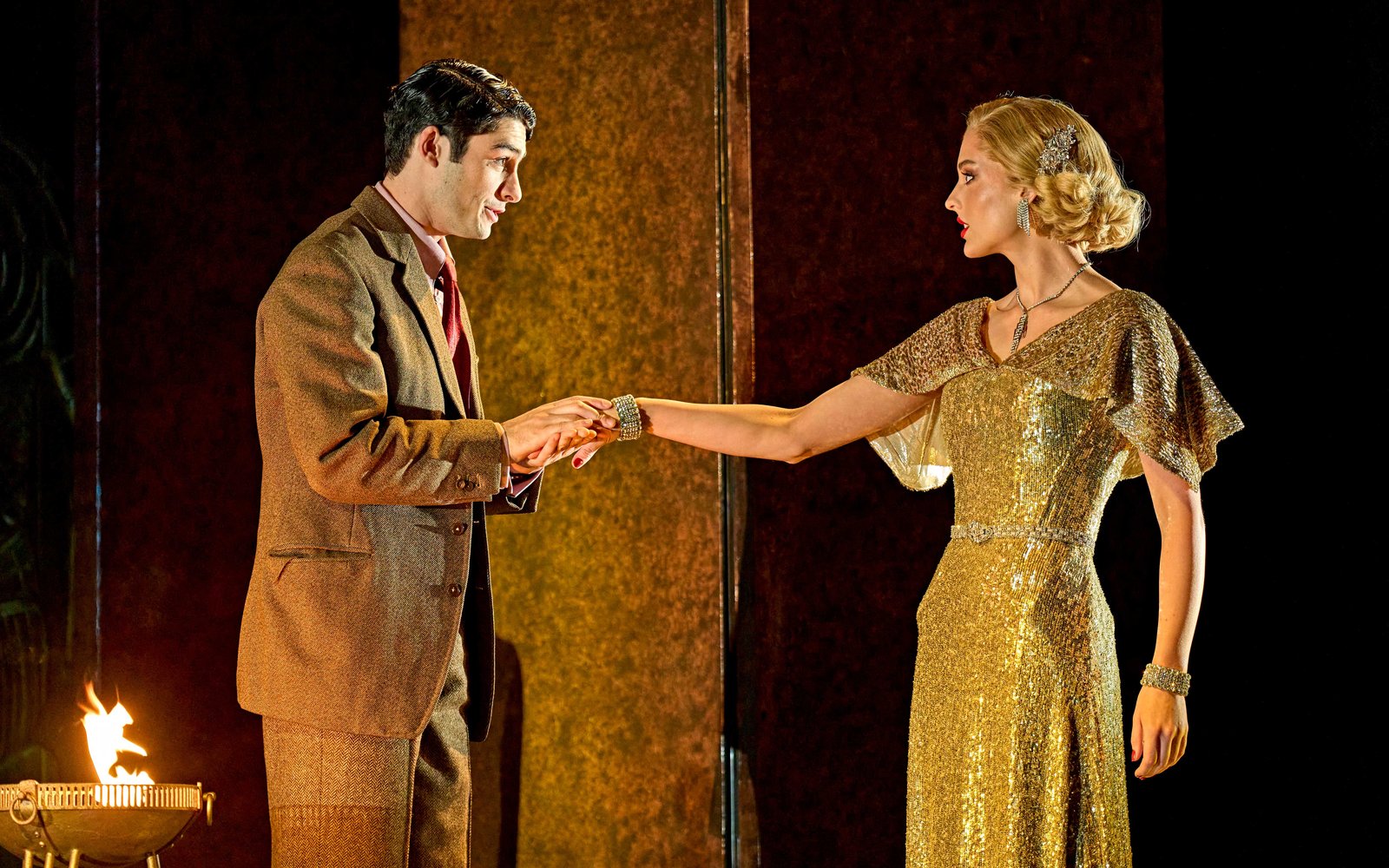A glamorous woman in a gold sequin dress holds her hand out to a man in a brown suit