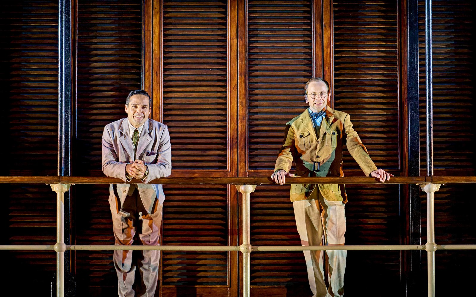 Two men in suits stand and look out over a boat's edge towards the camera