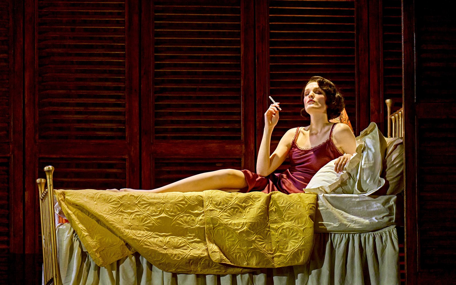 A woman in a red nightdress lies in bed seductively smoking a cigarette