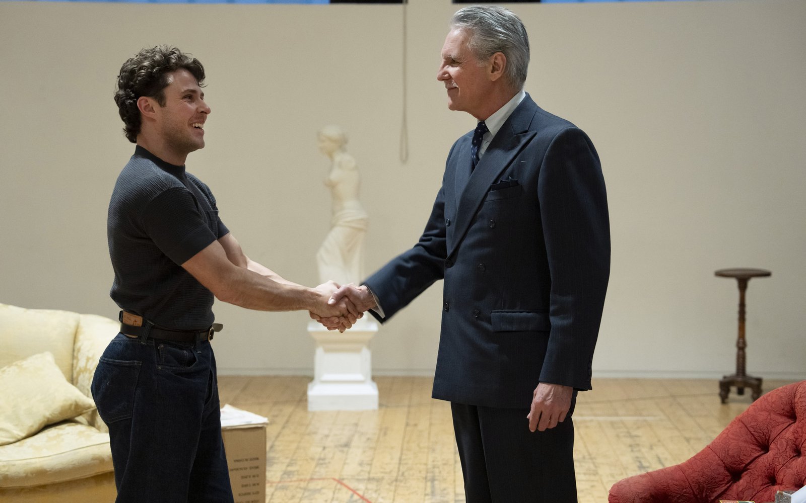 Two men shake hands, smiling at each other