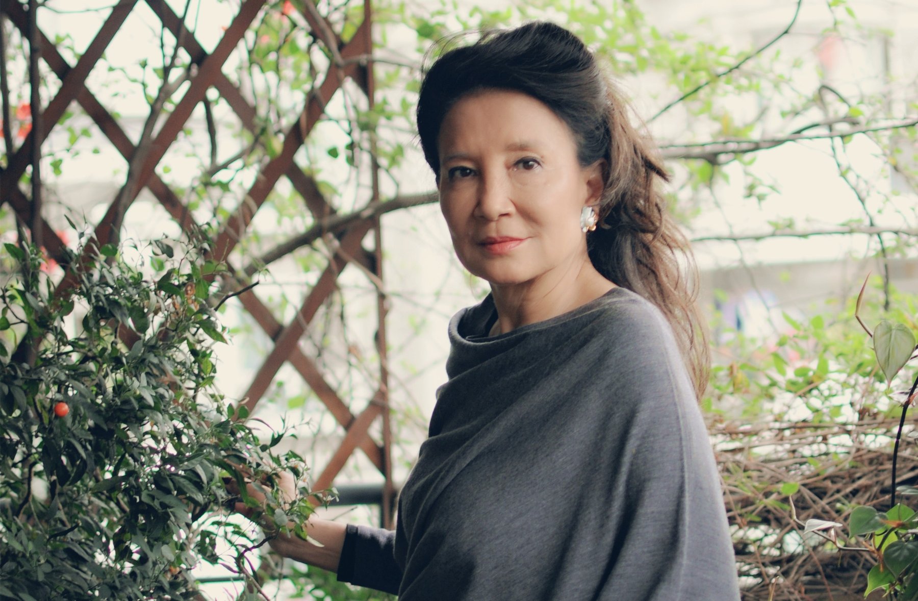 An Asian woman with long black hair stands in casual dress outside