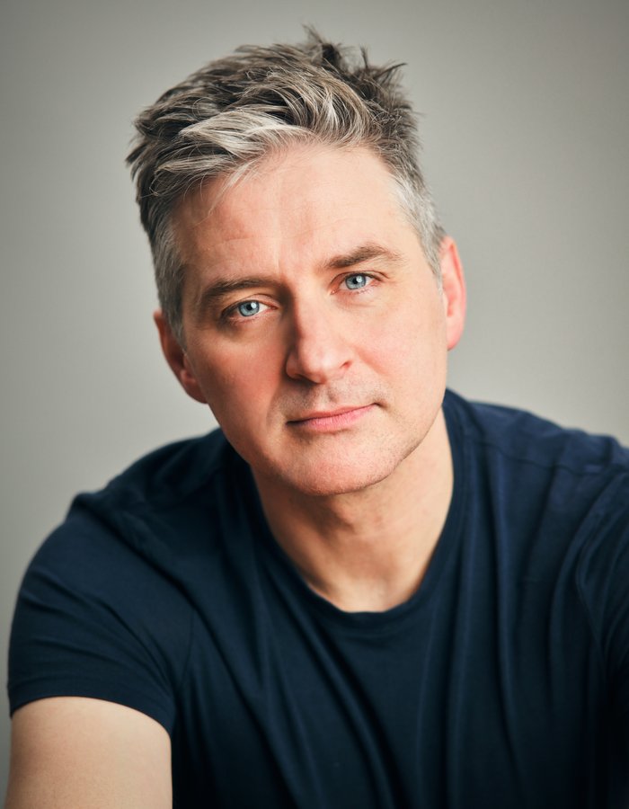 A man with grey hair and blue eyes wearing a blue tshirt