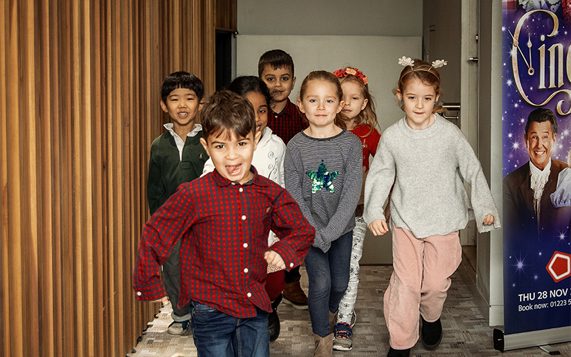 A group of children run towards the camera next to a Christmas tree.