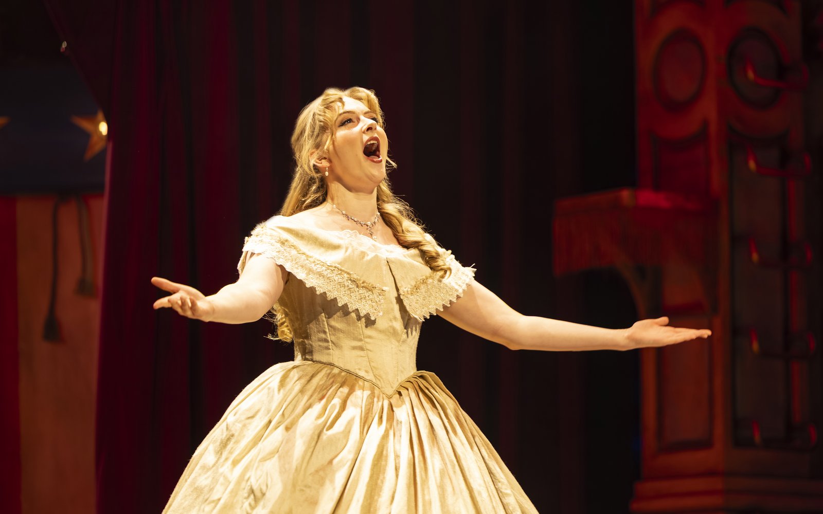 A woman in a glamorous dress sings with her arms outstretched