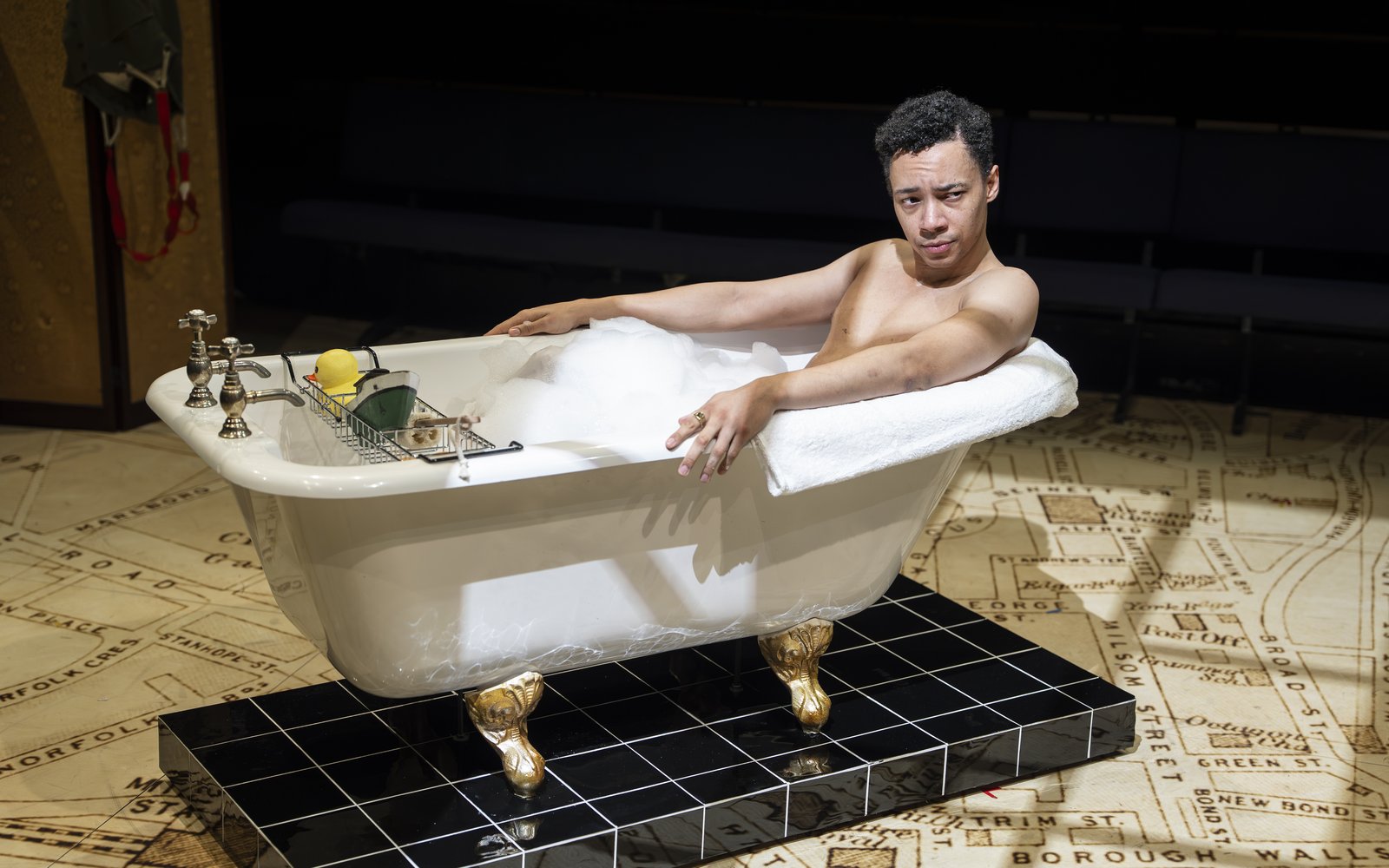 Kit Young lies in an old-fashioned bathtub filled with bubbles. He is looking out, one eyebrow raised.