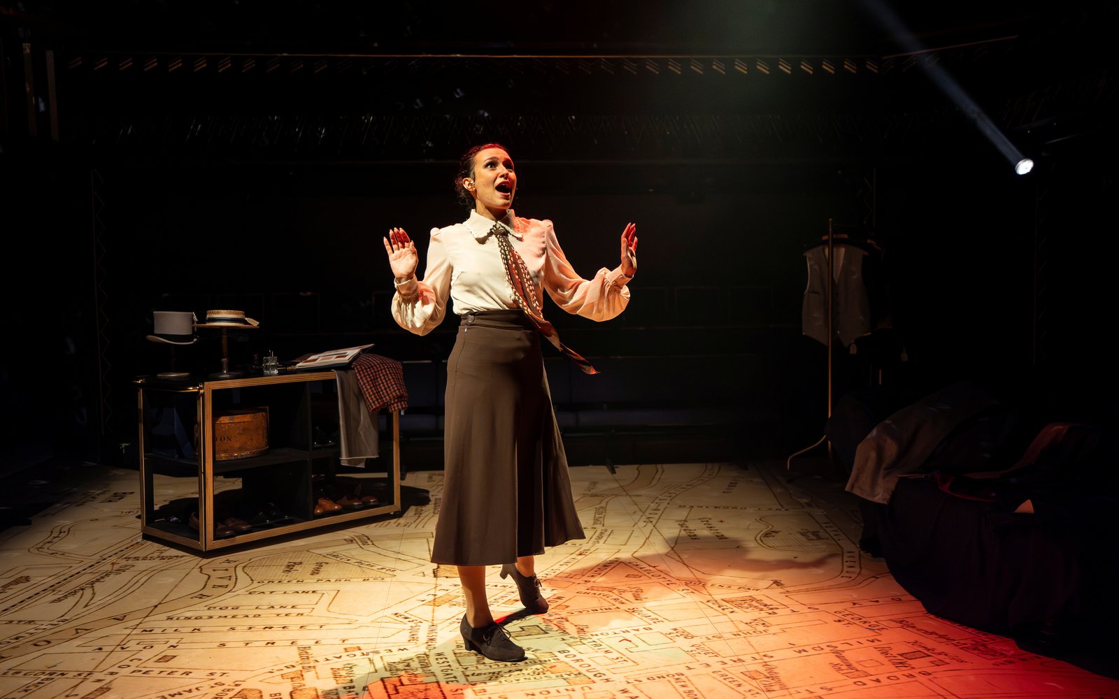 A woman in a long skirt, shirt and tie stands in the middle of the stage.