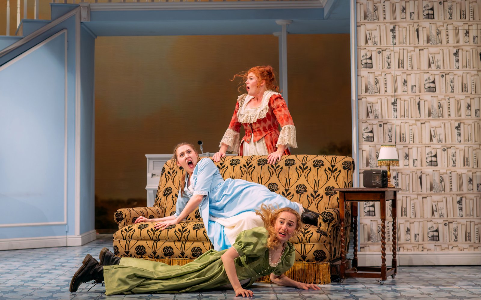 Three women lay across and around a sofa looking shocked