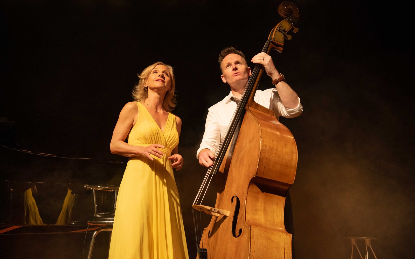 A man stands with a cello and a woman in a yellow dress stands next to him