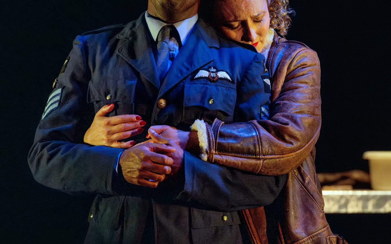 A woman hugs a man from behind. The man is wearing a World War 2 RAF uniform.