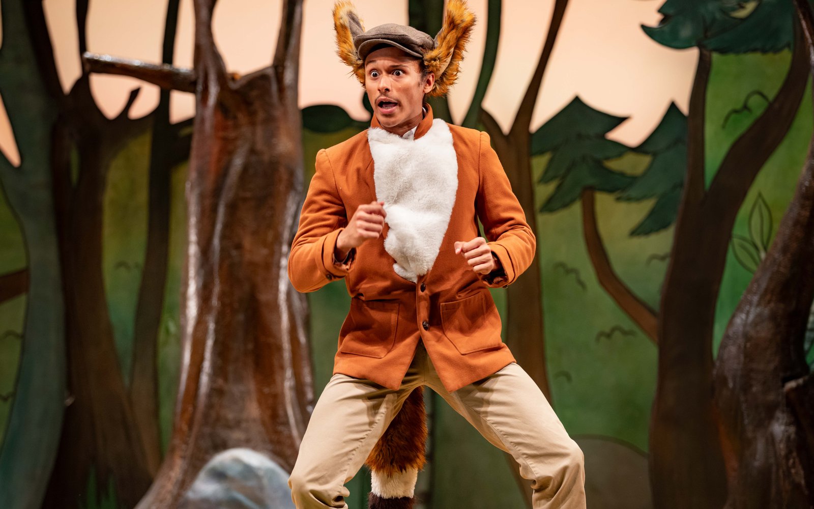 A man in an orange jacket and fluffy fox ears and a tail