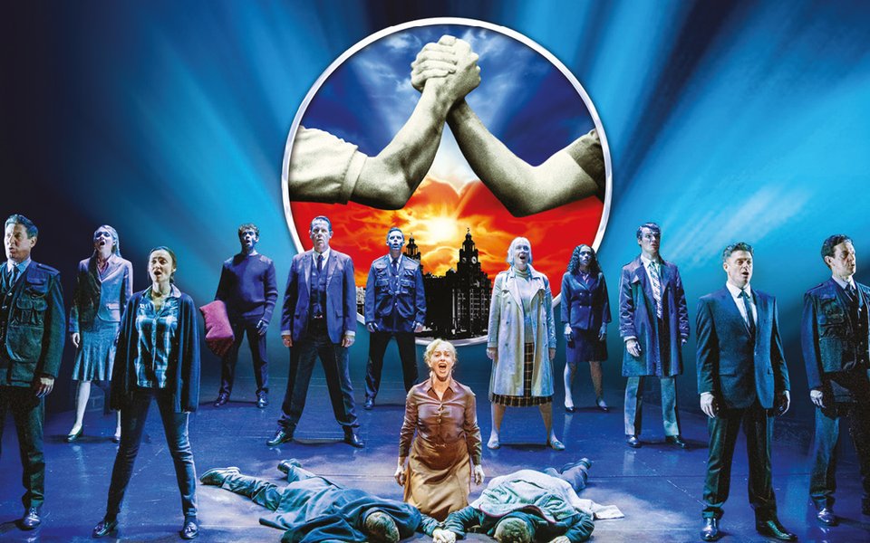 A stage with a group of people standing on it. At the front of the stage there are two boys on the ground and their mother stands over them.