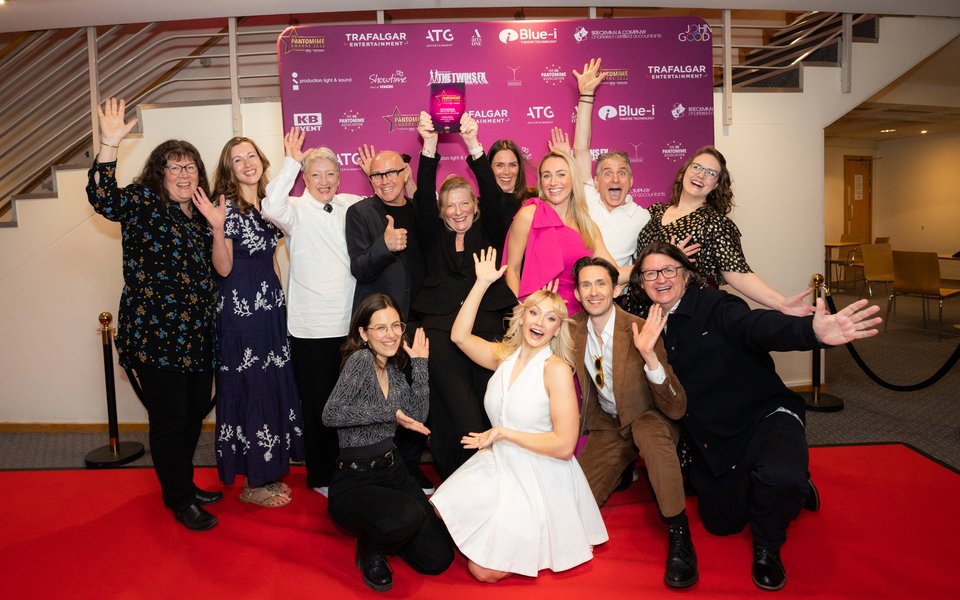 A group of people stood together smiling with their arms in the air, one woman is holding an Award